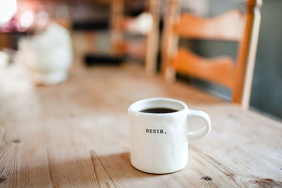 A white mug inscribed with the word "begin" sitting on a wooden table