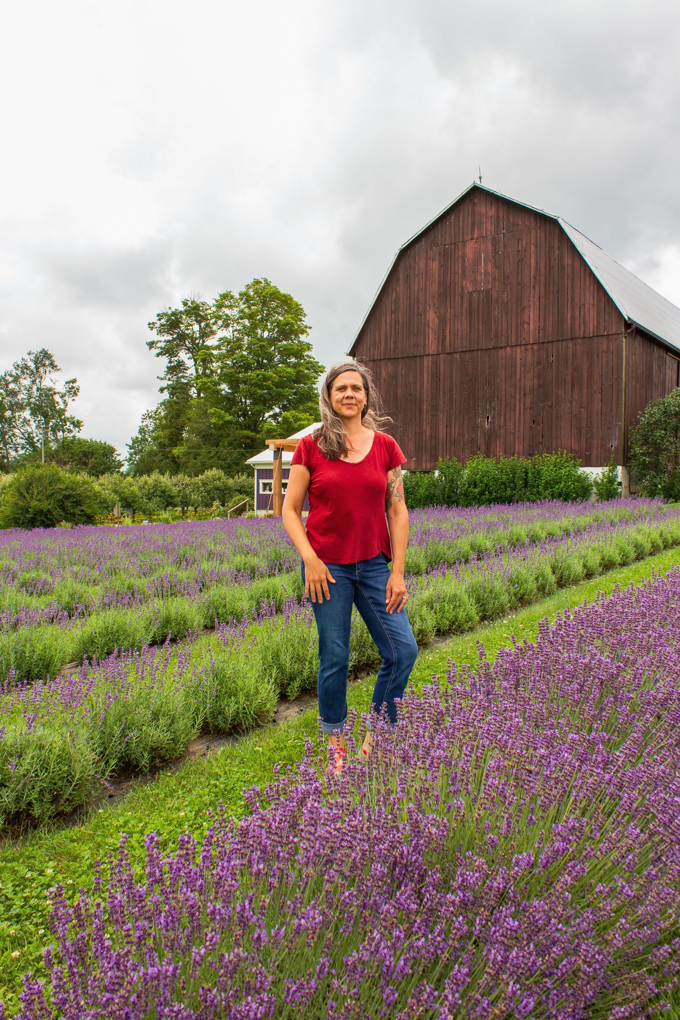 Melissa Schooley of The Raging Bowl Pottery stands in a field of lavender. Behind her is a large brown barn.