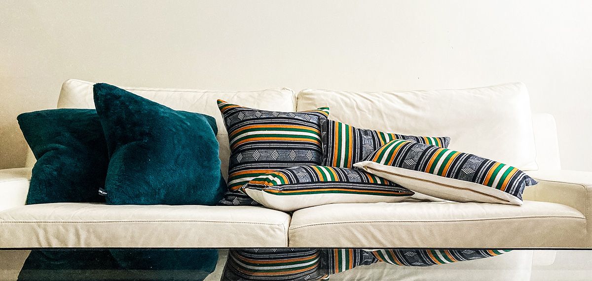 A white couch covered in two types of throw cushions: blue velvet, and striped and patterned in gold, green and grey.