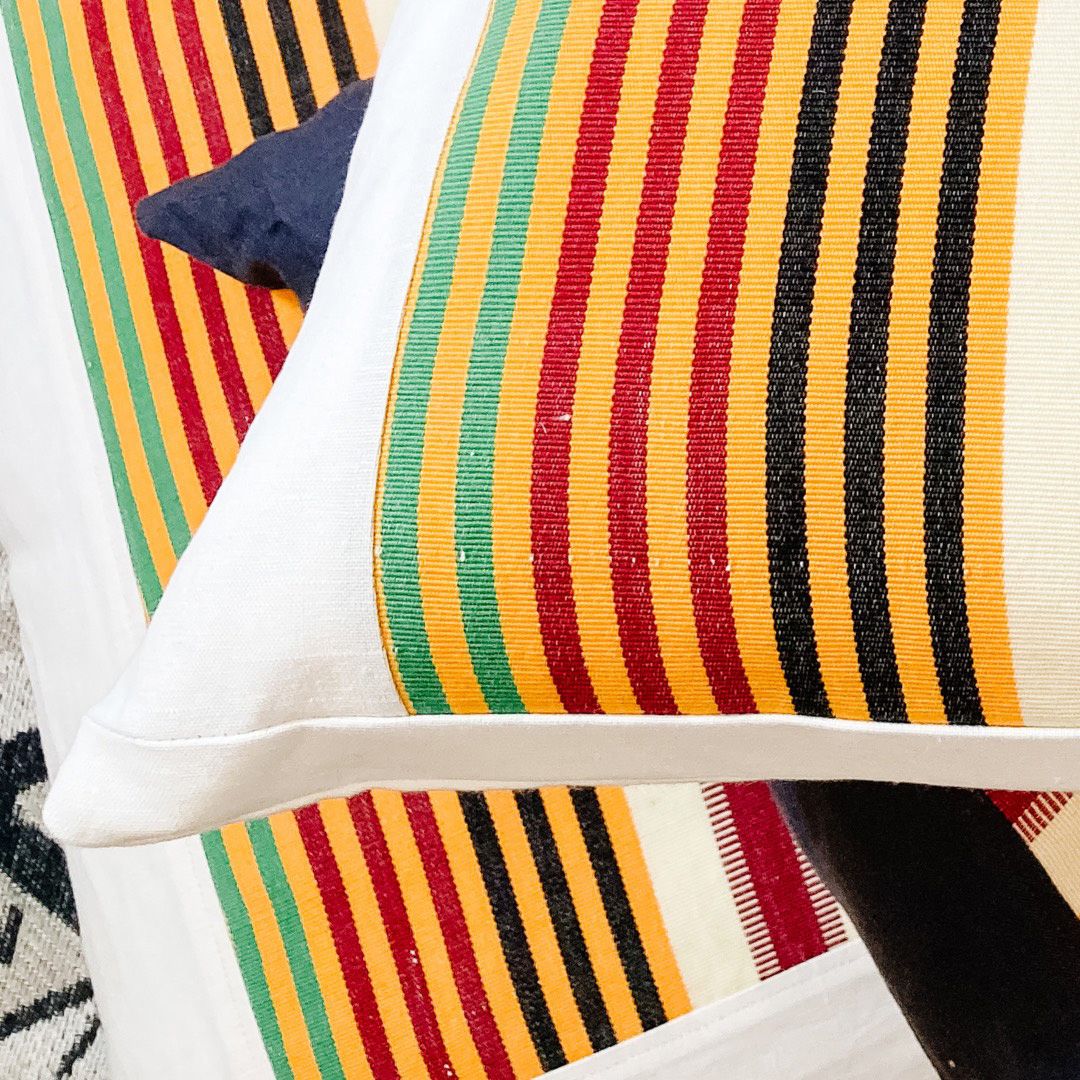 A stack of throw cushions made with a combination of white fabric and fabric in gold, green, red and black stripes.