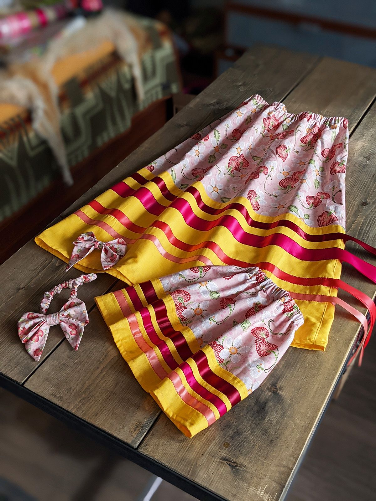 Two pink and yellow ribbon skirts, made with Indigenous Nouveau strawberry-patterned fabric, lying on a table.