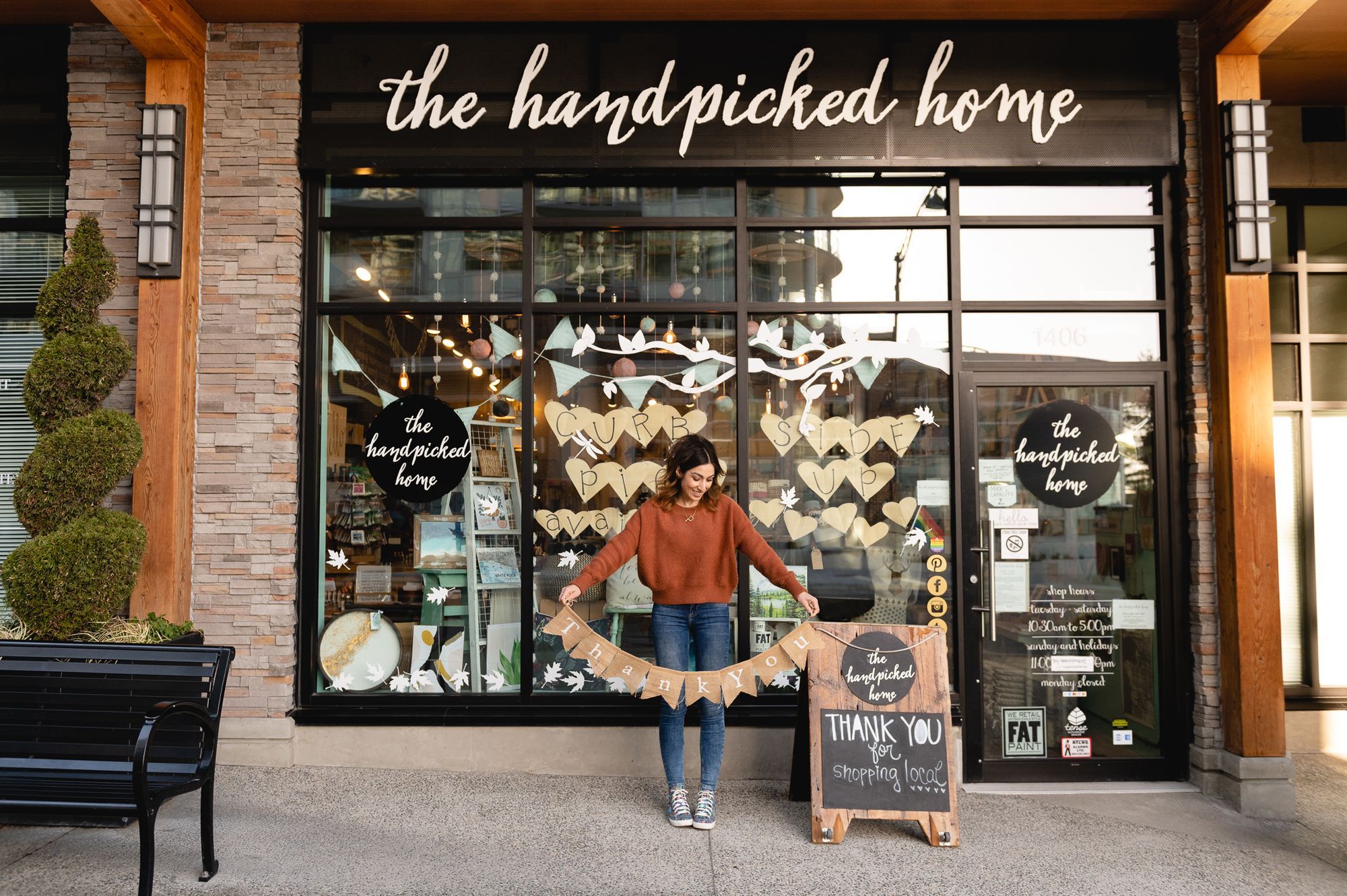 The storefront of The Handpicked Home, with owner Piya Sandhu standing in front holding a "thank you" banner.