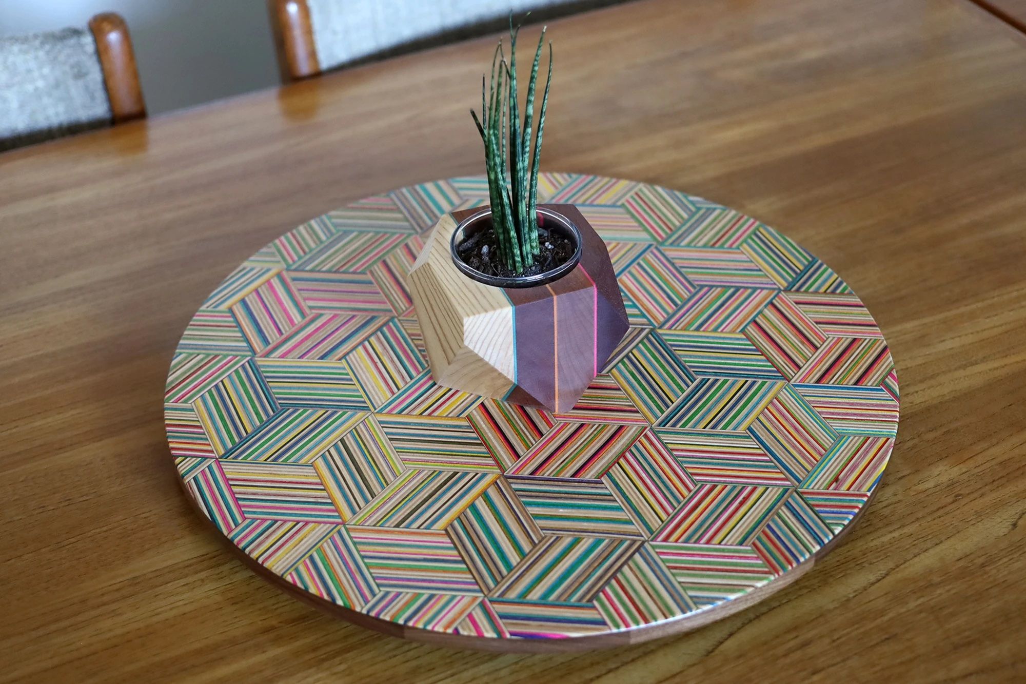 A colourful lazy susan made from upcycled skateboards on a wooden table with a plant on top.