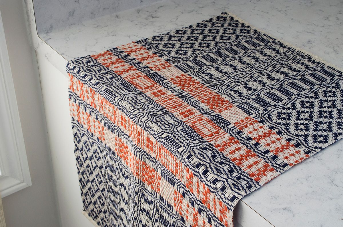 A hand-woven textile in navy, red and cream displayed on a counter.