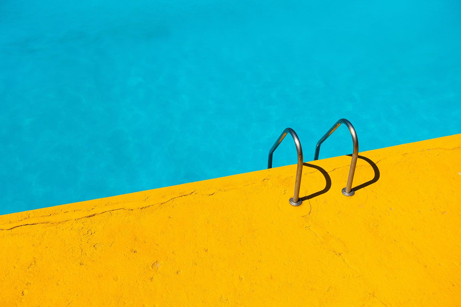A bright blue swimming pool with a ladder leading to a bright-yellow pool deck.