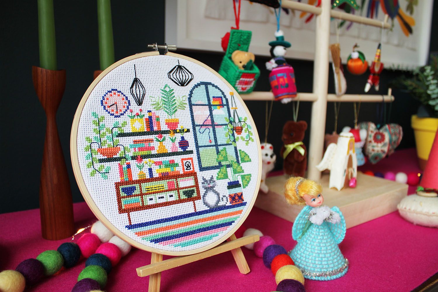 A framed cross-stitch on a table alongside colourful Christmas decorations