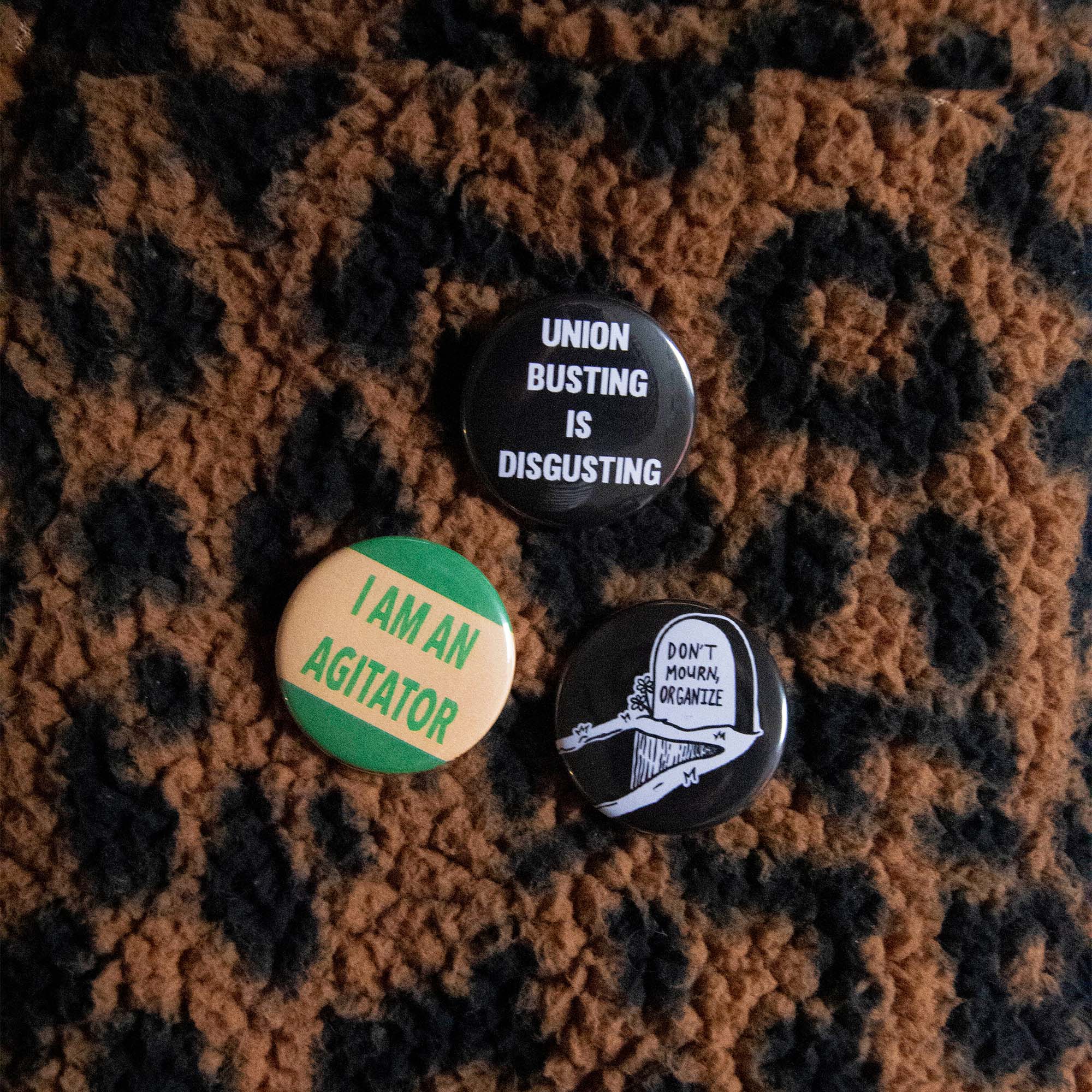 Three pins on a rug. 1. I am an agitator, 2. Don't mourn, organize, 3. Union busting is disgusting