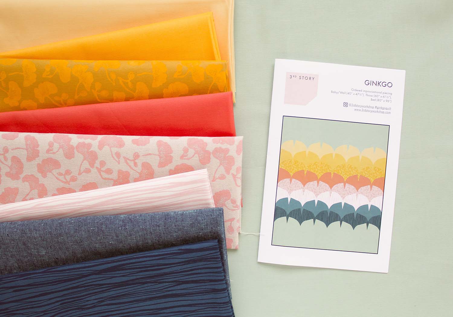 A stack of coloured fabric next to a quilt pattern