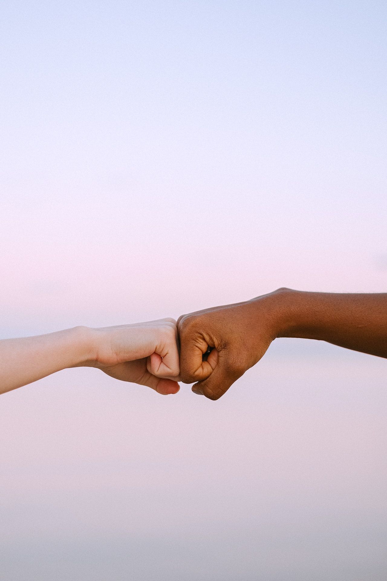 Two hands fist-bump against a pink-lavender background.