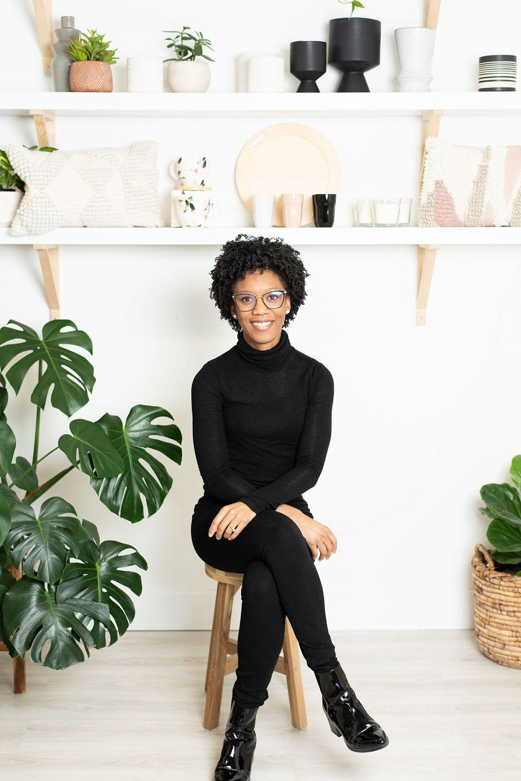 Nickeisha Lewis of Nola Designs sits on a wooden stool in front of shelves displaying homewares