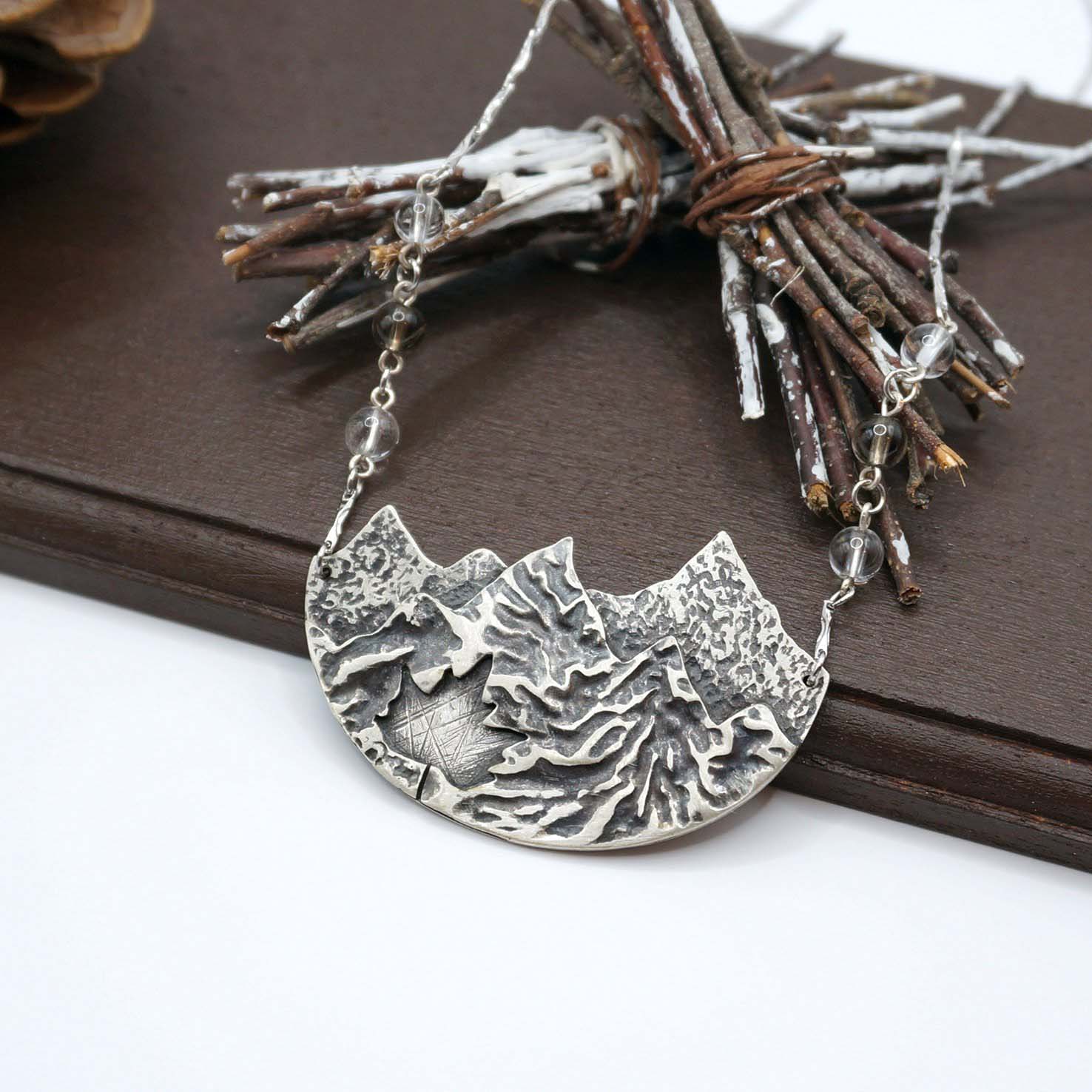 Silver necklace with mountains on a wooden platform with bundles of twigs