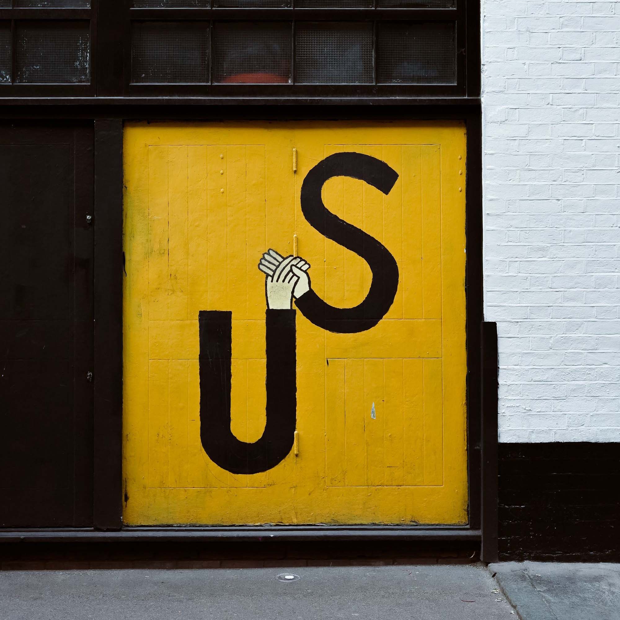 Yellow door with an illustration of the word "Us" with two hands holding