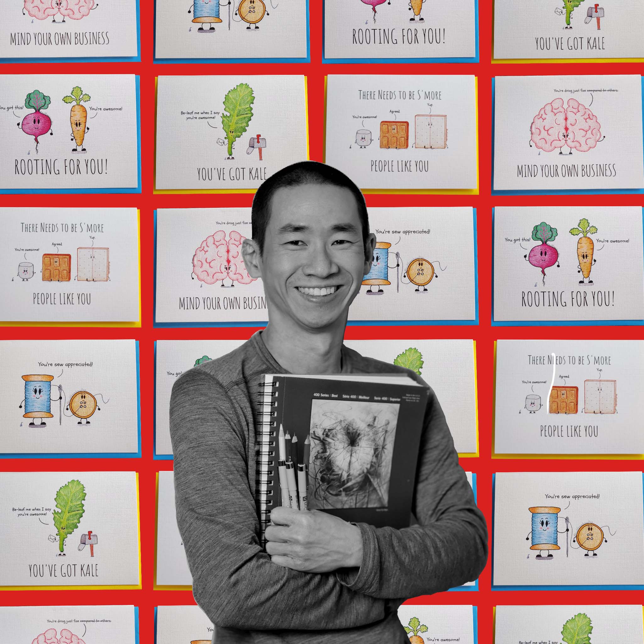 A person holding sketchbooks and pens in front of a collage of illustrated greeting cards