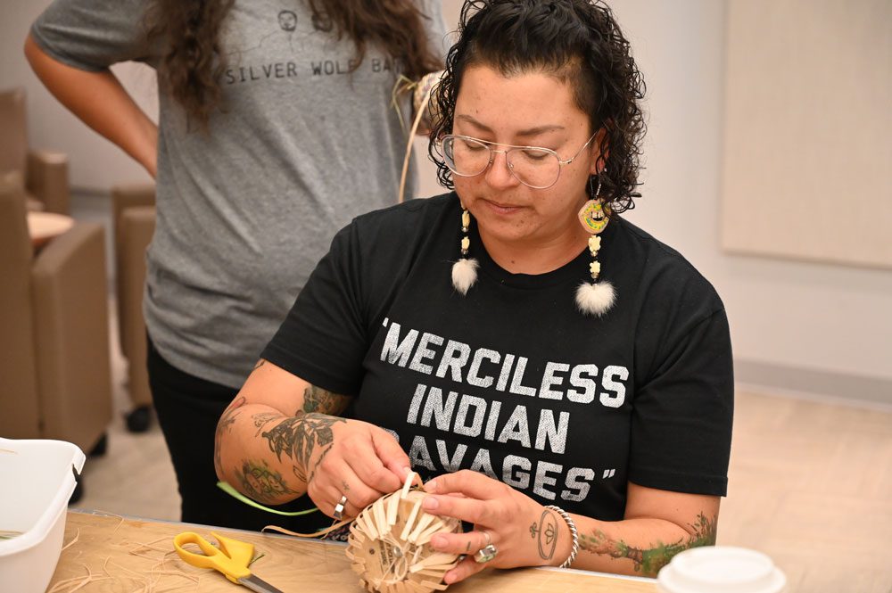 A person sitting at a table doing crafts, with another person standing behind