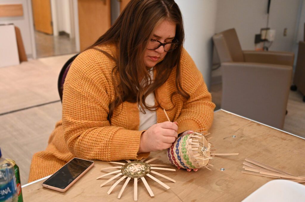 A person sitting at a table weaving a small basket