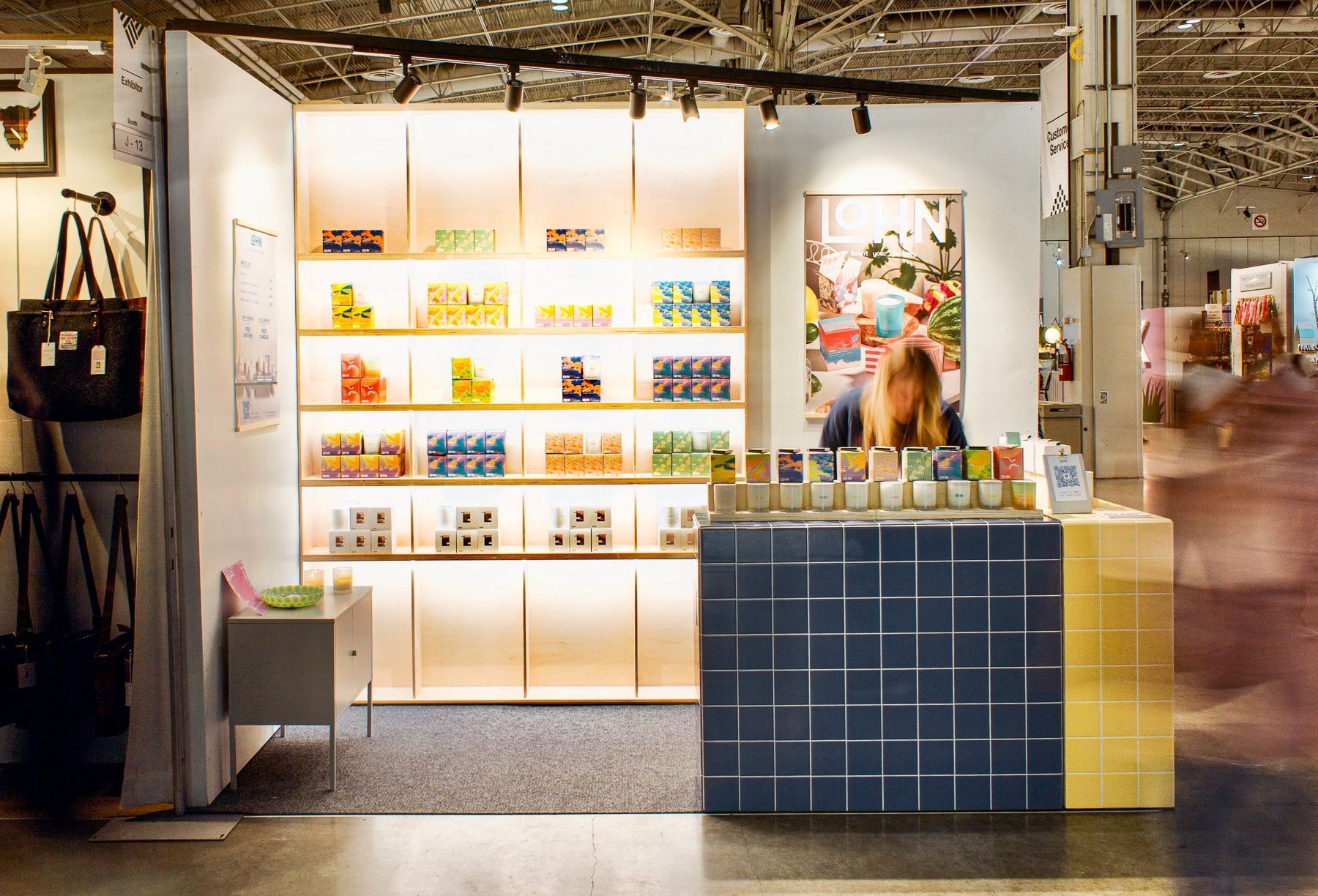 booth at a craft show with brightly lit shelves and a blue and yellow tiled cash desk