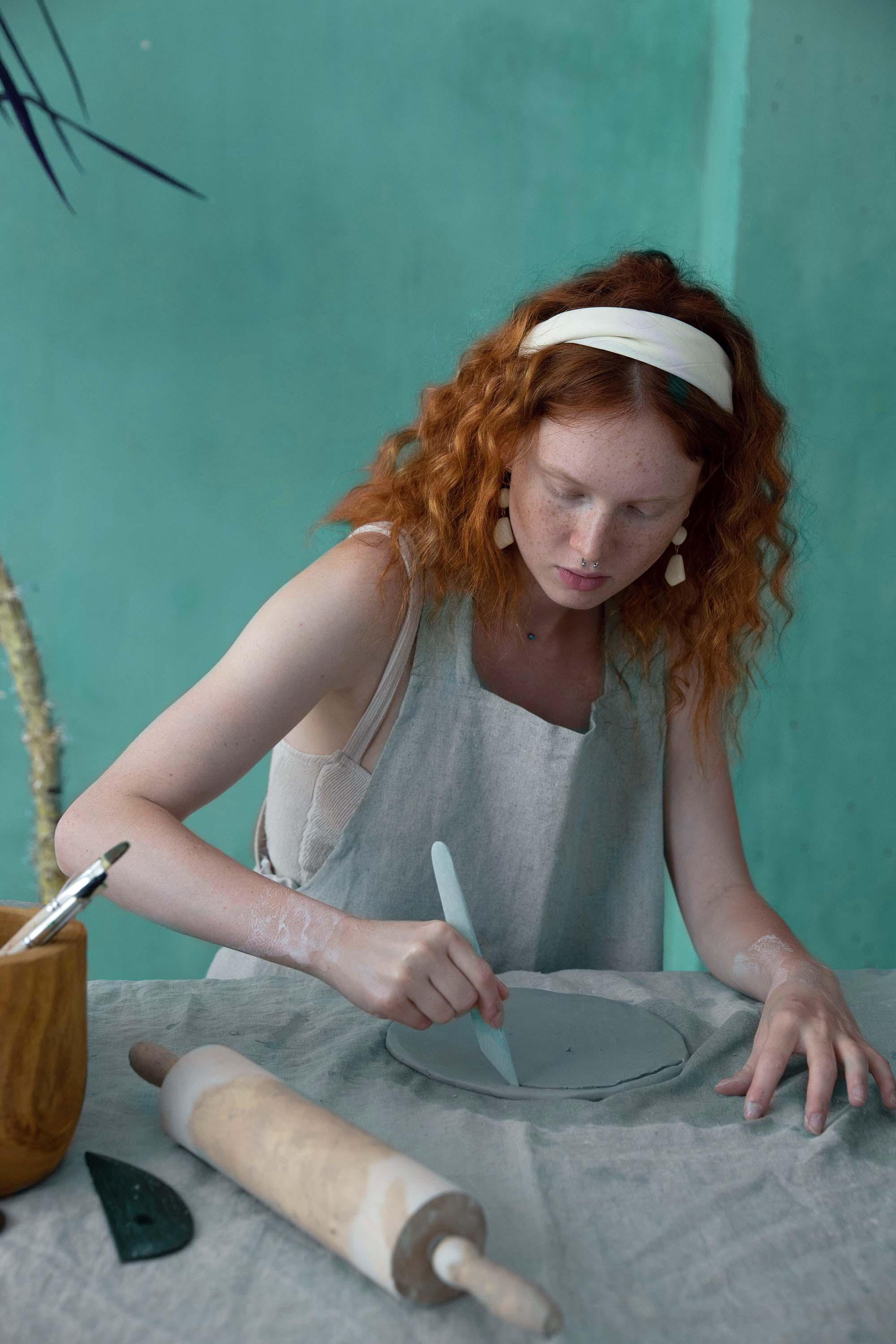 A person wearing an apron, working on a ceramics project in a studio